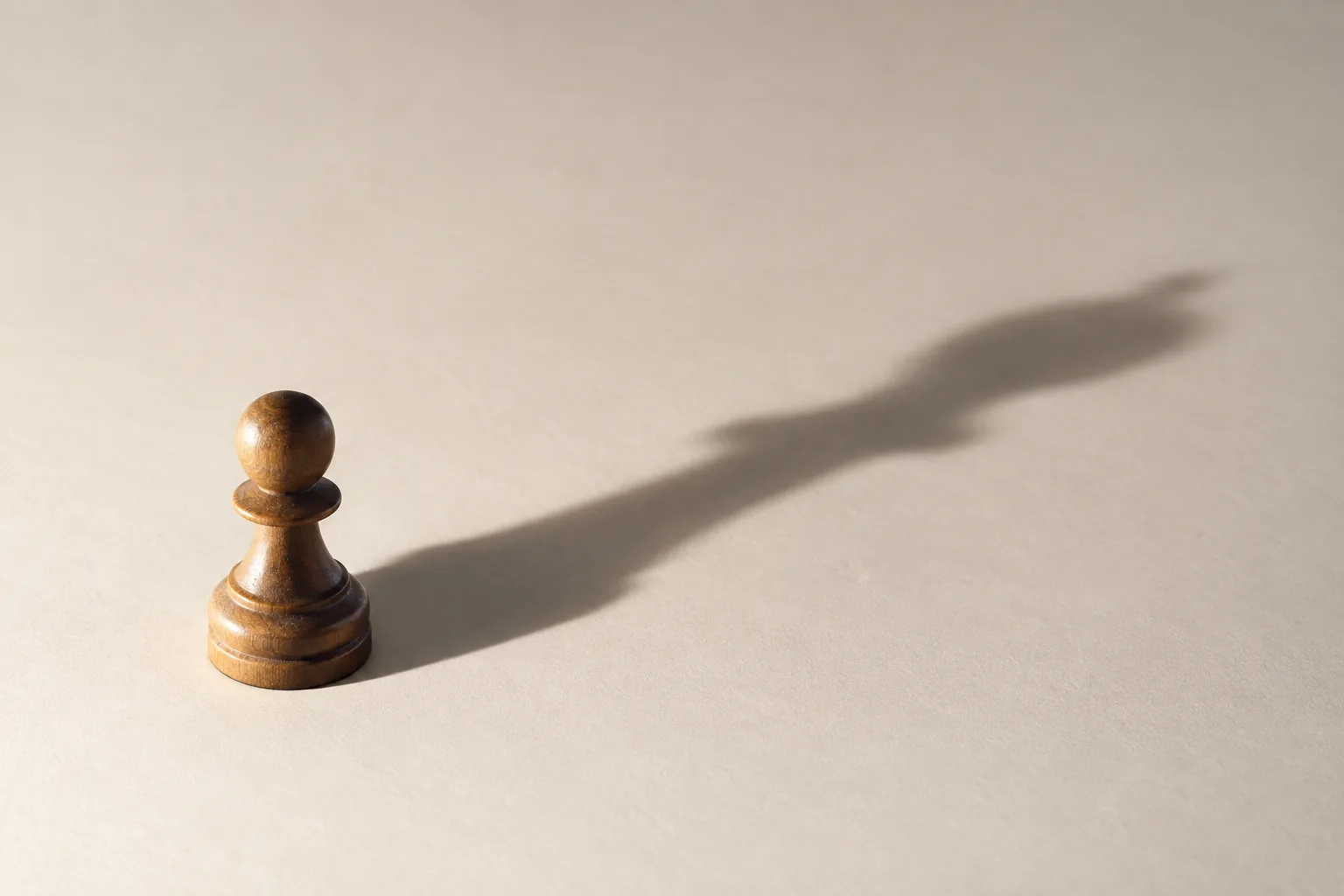 A small chess pawn casting a long, exaggerated shadow