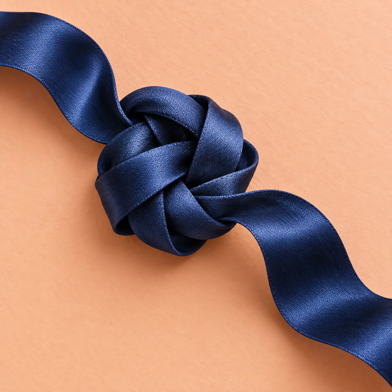 A navy satin ribbon tied in a knot on peach paper